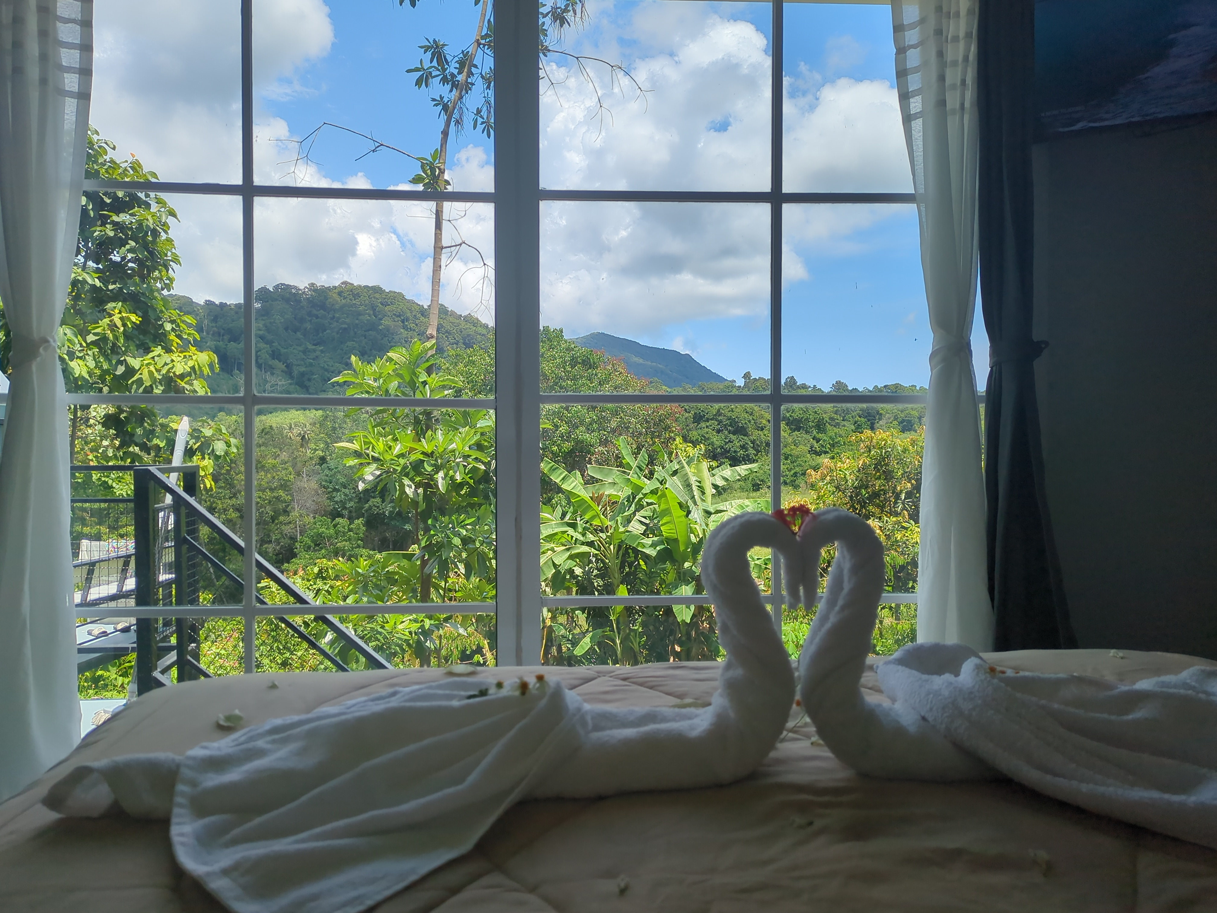 Bedroom interior with towel swans and jungle view through large windows